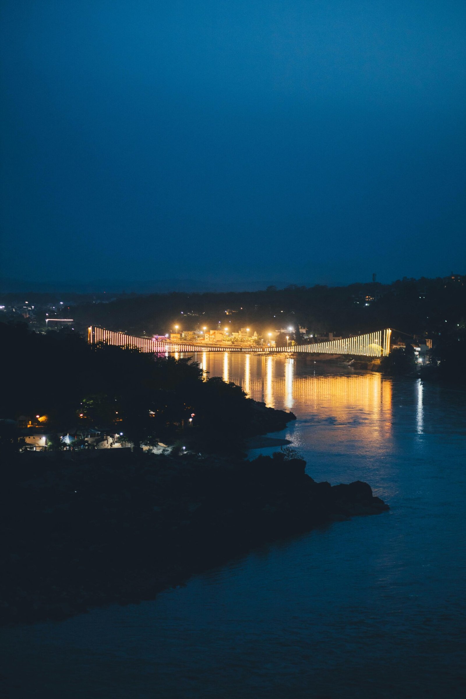 Beautiful night view of a suspension bridge over the Ganges River in Rishikesh, India, illuminated by lights.